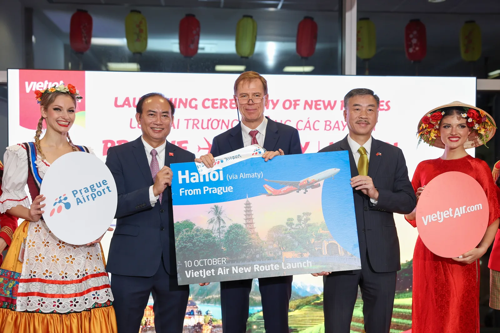 พิธีเปิดเส้นทาง Hanoi (via Almaty) จากปรากของ VietJet Air ผู้ร่วมพิธีถือป้ายเส้นทางใหม่ ข้างป้าย Prague Airport และ vietjetair.com