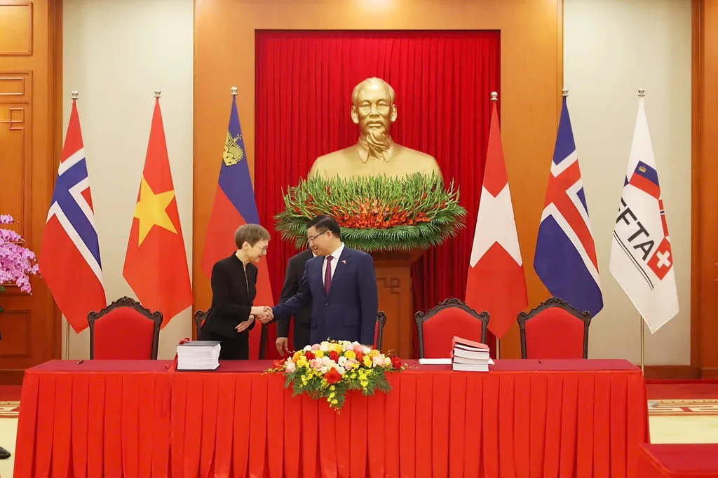 ผู้แทน EFTA และรัฐมนตรีการค้าเวียดนามจับมือกันหลังพิธีลงนามความตกลงการค้าเสรีที่ฮานอย 18 ตุลาคม 2026 ด้านหลังเป็นธงนอร์เวย์ เวียดนาม ลิกเตนสไตน์ สวิตเซอร์แลนด์ ไอซ์แลนด์ และธง EFTA