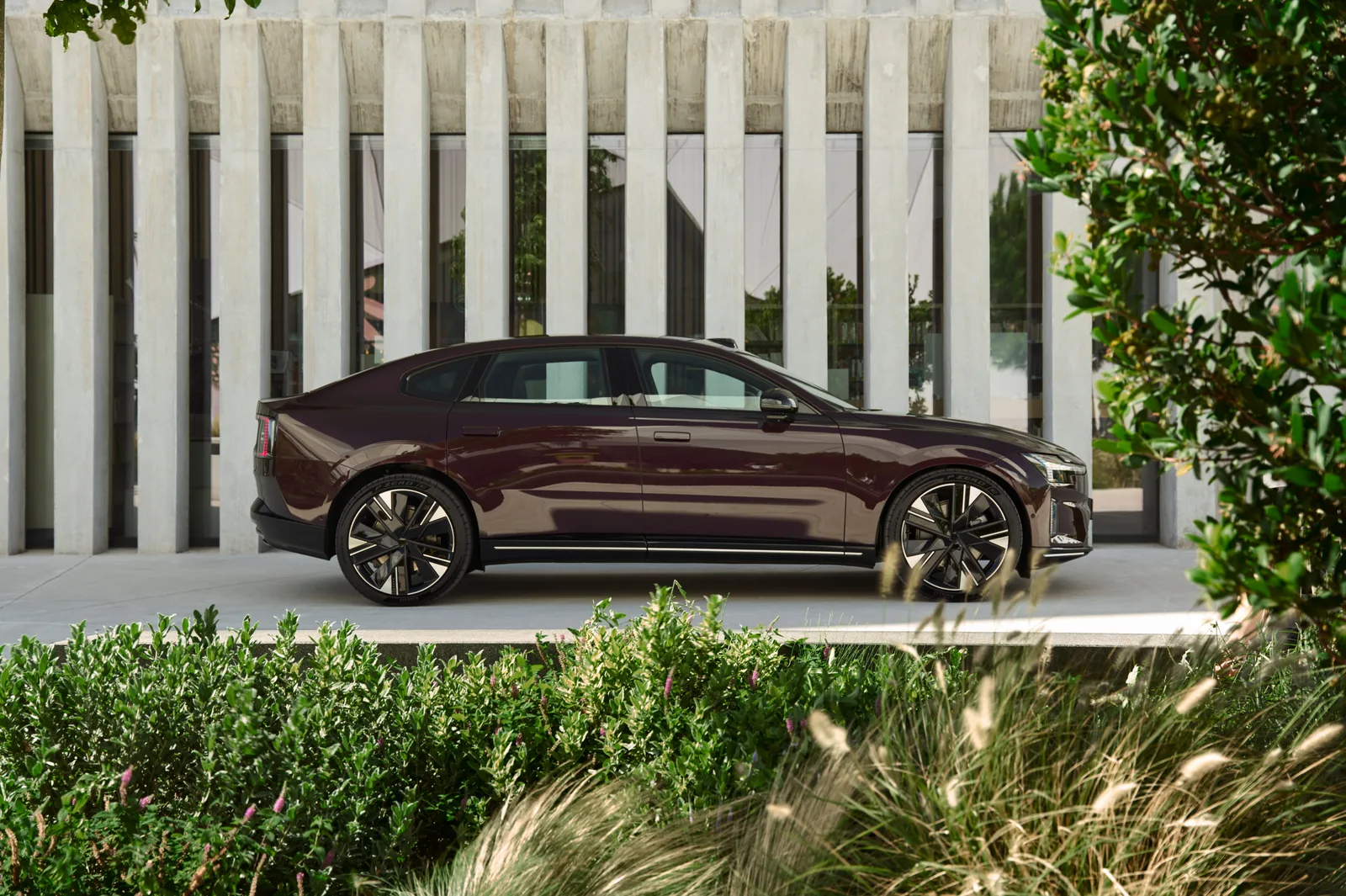 Volvo ES90 สีม่วงเข้มมุมด้านข้างจอดหน้าอาคารเสาคอนกรีต