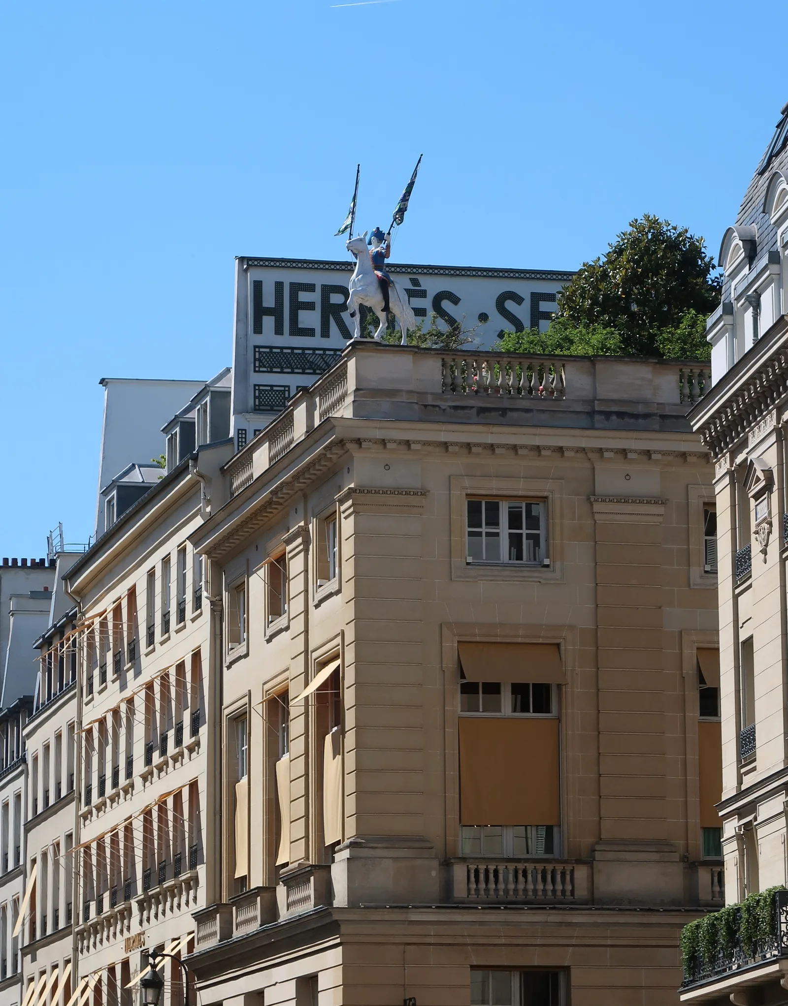 อาคาร Hermès เลขที่ 24 ถนน Faubourg Saint-Honoré ปารีส มีป้าย Hermès Sellier และรูปปั้นคนขี่ม้าถือธงบนหลังคา