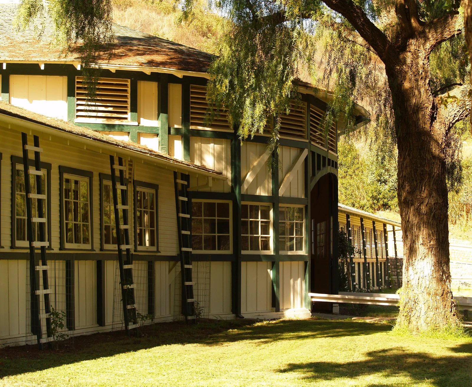 ด้านหน้าคอกม้าประวัติศาสตร์ของ Will Rogers Ranch ผนังไม้สีขาวคาดเส้นสีเขียว บันไดไม้สำหรับไม้เลื้อยพาดผนัง ภาพถ่ายเมื่อ 20 ตุลาคม 2006
