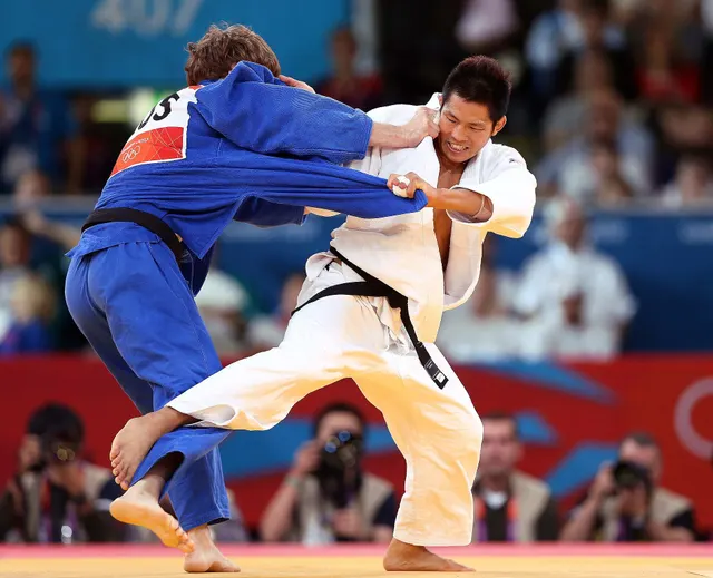 นักยูโดสองคนจับคู่กันบนเสื่อในโอลิมปิกลอนดอน 2012 คนหนึ่งสวมชุดยูโดสีขาวคาดเข็มขัดดำ อีกคนสวมชุดสีน้ำเงินคาดเข็มขัดดำ
